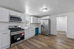 Kitchen with a textured ceiling, hardwood / wood-style floors, stainless steel appliances, sink, and white cabinetry