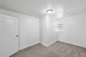 Empty room with light colored carpet and a textured ceiling