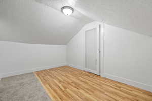 Bonus room featuring lofted ceiling, hardwood / wood-style flooring, and a textured ceiling