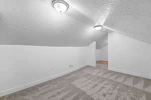 Bonus room featuring lofted ceiling, light carpet, and a textured ceiling