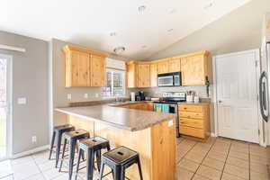 Kitchen with appliances with stainless steel finishes, vaulted ceiling, a breakfast bar area, and kitchen peninsula