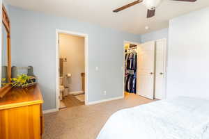 Carpeted bedroom featuring connected bathroom, a walk in closet, and ceiling fan