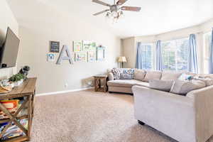 Living room with lofted ceiling, ceiling fan, and carpet flooring