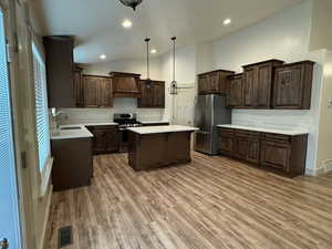 Kitchen featuring a center island, sink, stainless steel appliances, hardwood / wood-style floors, and decorative light fixtures