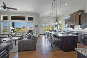 Kitchen with a kitchen island with sink, dark stone counters, ceiling fan with notable chandelier, and dark hardwood / wood-style floors