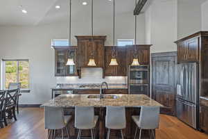 Kitchen with high vaulted ceiling, hardwood / wood-style floors, light stone counters, sink, and appliances with stainless steel finishes