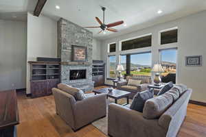 Living room with ceiling fan, a stone fireplace, light wood-type flooring, and beam ceiling