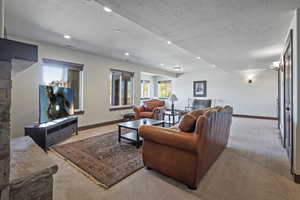 Living room with a stone fireplace, a textured ceiling, and carpet floors