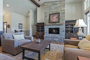 Living room with hardwood / wood-style floors, high vaulted ceiling, beamed ceiling, and a stone fireplace