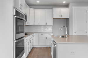 Kitchen with a kitchen island with sink, light hardwood / wood-style flooring, sink, appliances with stainless steel finishes, and white cabinets