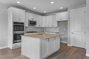 Kitchen featuring a center island with sink, stainless steel appliances, white cabinets, and light hardwood / wood-style floors