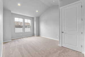 Unfurnished room featuring light colored carpet and vaulted ceiling