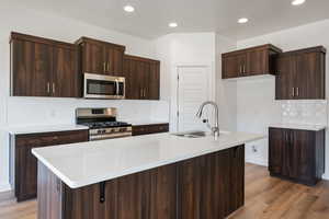 Kitchen featuring stainless steel appliances, a center island with sink, dark brown cabinetry, and sink