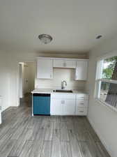 Kitchen featuring stainless steel dishwasher, white cabinets, light hardwood / wood-style flooring, and sink