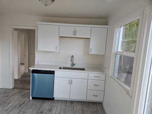 Kitchen featuring white cabinetry, stainless steel dishwasher, sink, and light wood-type flooring