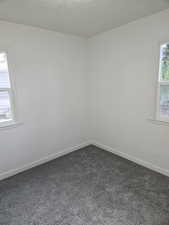 Empty room with dark carpet, a textured ceiling, and a healthy amount of sunlight