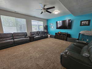 Living room featuring ceiling fan, carpet, and a textured ceiling