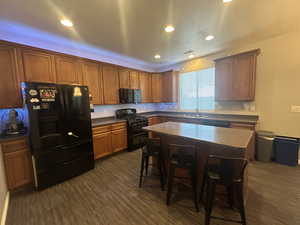 Kitchen with a center island, a breakfast bar area, sink, black appliances, and dark hardwood / wood-style flooring