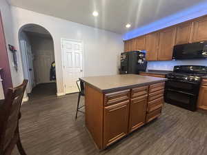 Kitchen with black appliances, a kitchen bar, dark wood-type flooring, and a center island