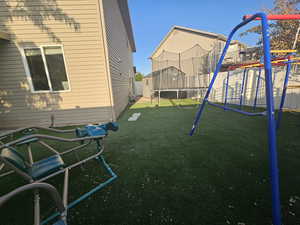 View of playground featuring a trampoline and a yard