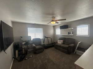 Carpeted living room with ceiling fan and a textured ceiling