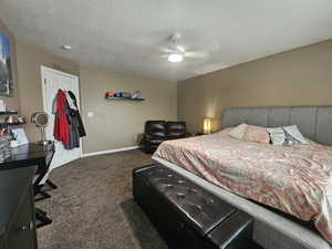 Bedroom with ceiling fan, a textured ceiling, and dark colored carpet