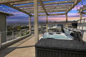 Night view of rooftop deck with pergola, string lights, Bullfrog hot tub, and gas line for BBQ