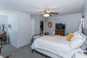 Carpeted bedroom with ceiling fan, a closet, a walk in closet, and a textured ceiling