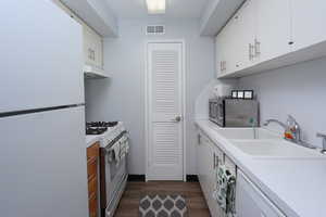 Kitchen with sink, dark hardwood / wood-style flooring, white appliances, and white cabinets