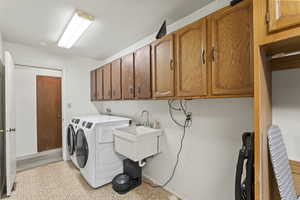 Clothes washing area with cabinets, washing machine and clothes dryer, and sink