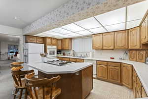 Kitchen with white appliances, a kitchen bar, a center island, and sink