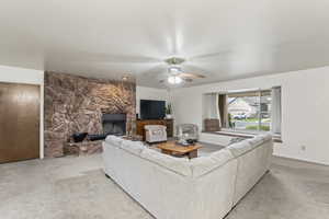 Living room with ceiling fan, carpet floors, and a fireplace