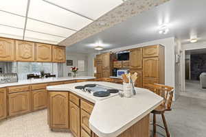 Kitchen featuring white appliances, a kitchen breakfast bar, kitchen peninsula, a center island, and light colored carpet