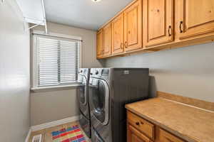 Clothes washing area with cabinets, washer and clothes dryer, and light tile patterned flooring