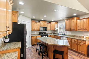 Kitchen featuring black appliances, a breakfast bar area, a center island, and dark hardwood / wood-style flooring