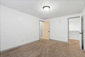 Unfurnished bedroom with a walk in closet, a textured ceiling, and carpet floors