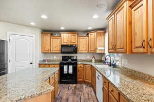 Kitchen with black appliances, sink, dark hardwood / wood-style floors, and light stone countertops