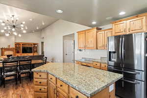 Kitchen featuring a notable chandelier, stainless steel fridge, a kitchen island, light stone countertops, and dark hardwood / wood-style floors