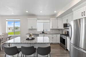 Kitchen with a center island, light stone counters, stainless steel appliances, and dark wood-type flooring