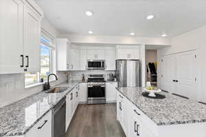 Kitchen featuring appliances with stainless steel finishes, light stone counters, sink, dark hardwood / wood-style floors, and a kitchen island