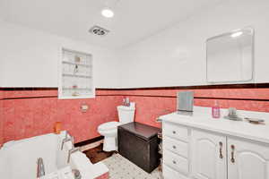 Bathroom featuring a tub, toilet, vanity, and tile walls