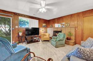 Living room with ceiling fan, wooden walls, and a fireplace