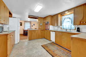 Kitchen with white appliances, backsplash, kitchen peninsula, and sink