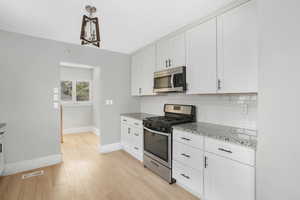 Kitchen with white cabinets, appliances with stainless steel finishes, pendant lighting, and light hardwood / wood-style flooring