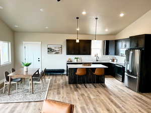 Kitchen featuring a kitchen island, appliances with stainless steel finishes, a sink, light countertops, and lofted ceiling