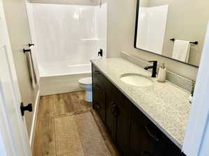 Full bathroom featuring toilet, shower / tub combination, wood finished floors, and vanity