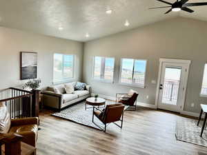 Living area with a healthy amount of sunlight, a ceiling fan, light wood-type flooring, and lofted ceiling