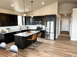 Kitchen with appliances with stainless steel finishes, a center island, light wood-type flooring, a sink, and light countertops