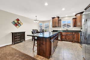 Kitchen with a kitchen island, a kitchen breakfast bar, an inviting chandelier, sink, and dark stone counters