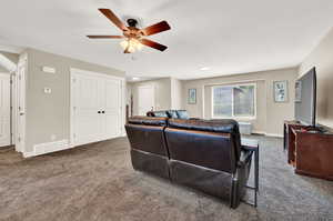 Living room with ceiling fan and dark colored carpet